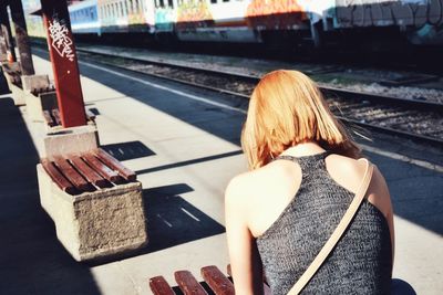 Rear view of woman sitting on railroad track