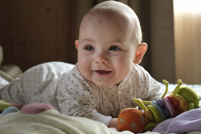 Smiling baby girl learning to crawl and playing with colorful toys in white sunny bedroom.