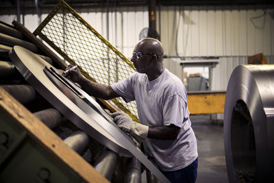 Side view of manual worker writing on rolled up sheet metals while working in industry