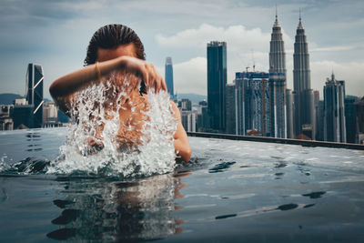 Woman by swimming pool against buildings in city