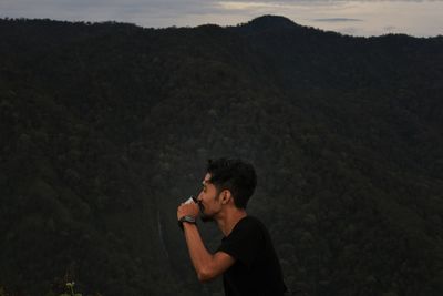 Side view of man drinking against mountains at dusk