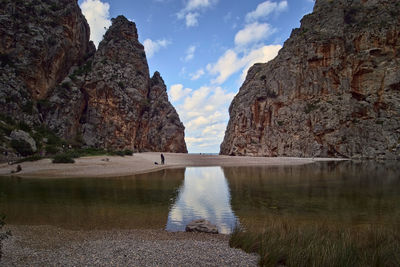 Rock formations by lake against sky