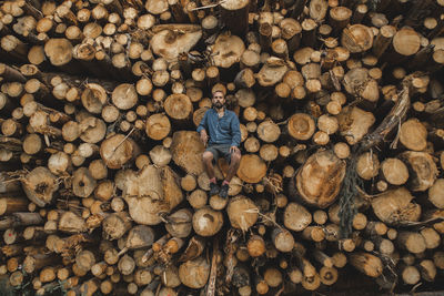 Man sitting on pile of logs at lumberyard