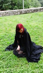 Woman wearing witch costume while sitting on grassy field