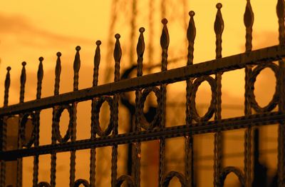 Close-up of metal fence against sky during sunset