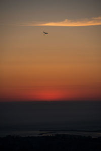 Silhouette bird flying in sky during sunset