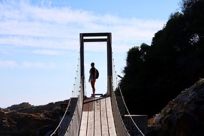 Full length of woman standing on rope bridge against sky