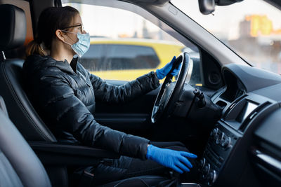 Woman with glasses, medical mask and latex gloves driving a car with her hands on the steering wheel