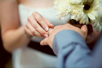 Midsection of woman putting ring in groom finger during wedding ceremony