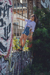 Young woman standing on window sill amidst graffiti wall