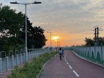People riding bicycle on road against sky during sunset