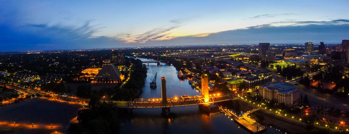 High angle view of illuminated city by river against sky