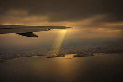 Airplane wing over sea against sky during sunset