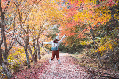 Rear view of man walking by trees in forest during autumn