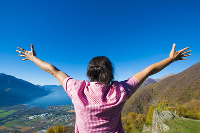 Rear view of woman with arms outstretched standing on mountain against clear blue sky