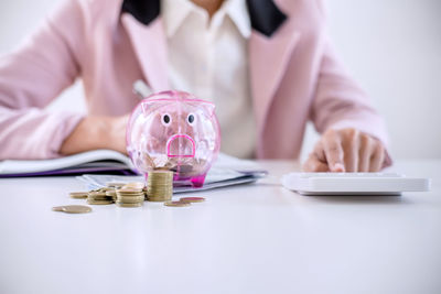 Midsection of businesswoman counting money with piggybank on table