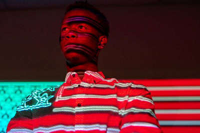 Serious african american male illuminated by red and blue neon projection of national american flag standing in dark studio