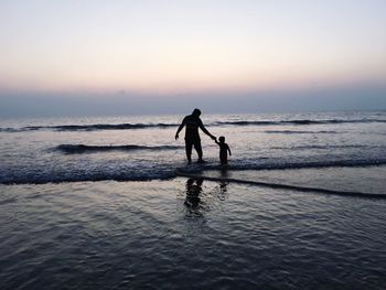 Silhouette of man with son walking on beach at sunset