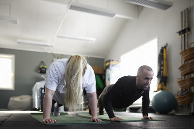 Smiling mid adult couple practicing plank position together at health club