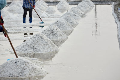 Worker using wooden rake for harvesting dried salt at salt pan