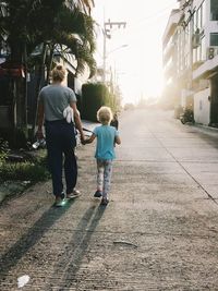 Rear view of mother and daughter walking on footpath in city