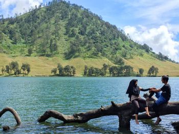 People sitting by lake against trees