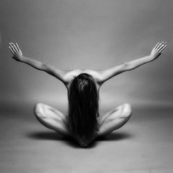 Naked woman sitting with arms outstretched against gray background