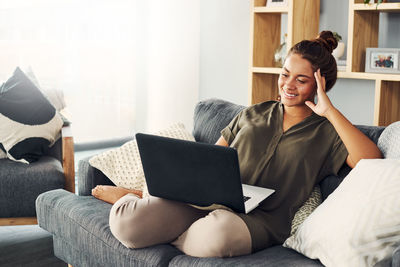 Young woman using phone while sitting on sofa at home