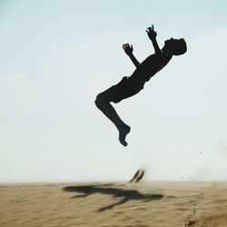 Silhouette mid adult man jumping on sand at beach against clear sky