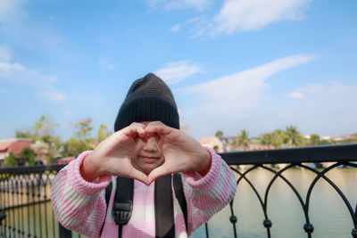 Girl making heart shape against sky