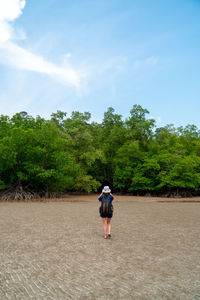 Rear view of man walking on dirt road against sky