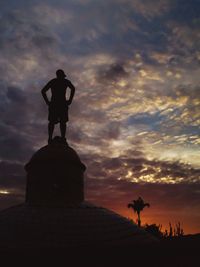 Rear view of man with hand on hip standing on dome against sky during sunset