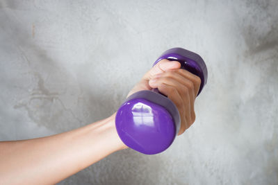 Cropped hand lifting purple dumbbell against wall