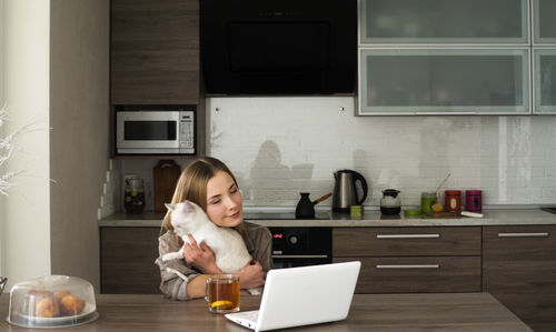 Woman hugging cat and using laptop