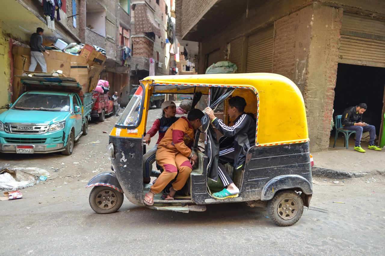 Cairo, egypt - december 14, 2019: side view of local folks chatting while driving tuk tuk car on dirty road of poor city district