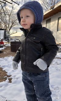 Cute baby boy looking away while standing on snow covered land