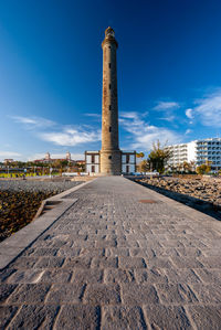 Road amidst buildings against blue sky