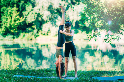 Women doing yoga by the water. instructor helping woman to do headstand.