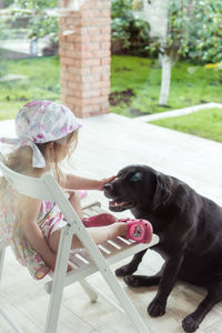 Little girl stroking a big black labrador retriever dog