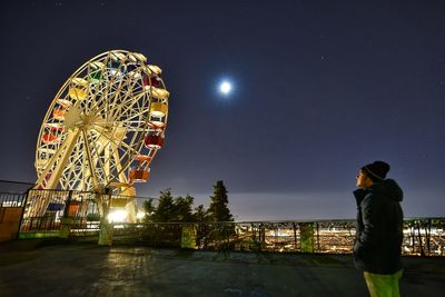 Side view of mature man looking at illuminated ferris wheel against sky