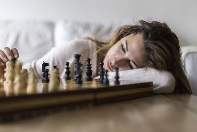 Young woman playing chess while lying on sofa