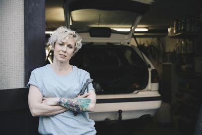 Portrait of confident female owner leaning on door at entrance of auto repair shop