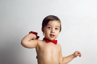 Child without a t-shirt sitting on a white background with a red bow tie