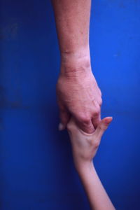 Cropped image of parent and baby holding hands against blue background