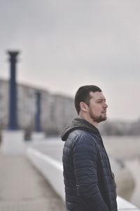 Side view of young man looking away against sky