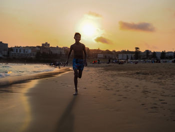 Full length of man on beach against sky during sunset