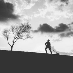 Silhouette man standing by tree against sky