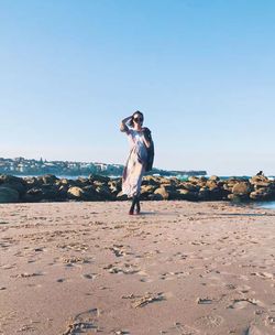 Full length of young woman standing on beach against clear blue sky