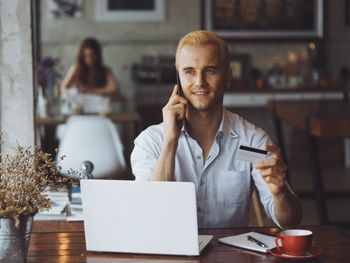 Young man holding credit card while talking on smart phone