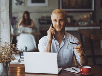 Smiling man holding credit card while talking on phone